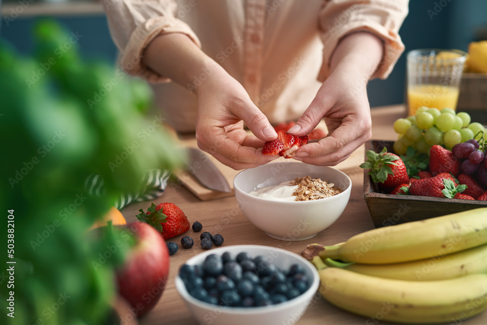 Woman making bowl full of yogurt with strawberries Woman making bowl full of yogurt with strawberries