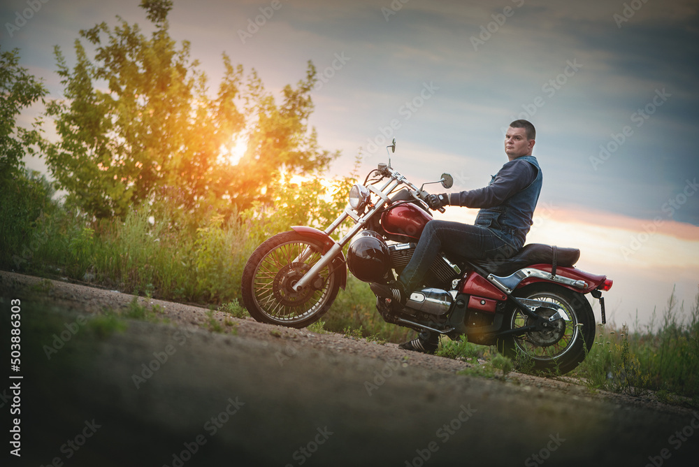 Fototapeta premium Motorcyclist is sitting on the motorbike outdoors at sunset.