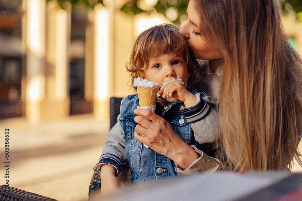 Male toddler getting kisses on the head from his mom while eating ice