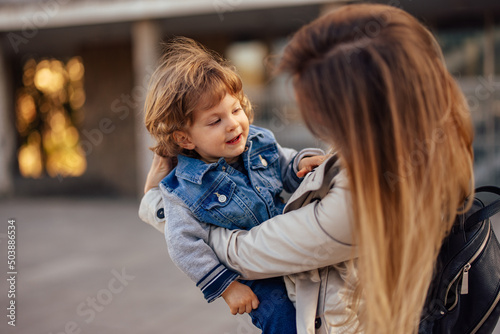 Photo of a cute smiling toddler, being held by his mom, outdoor.