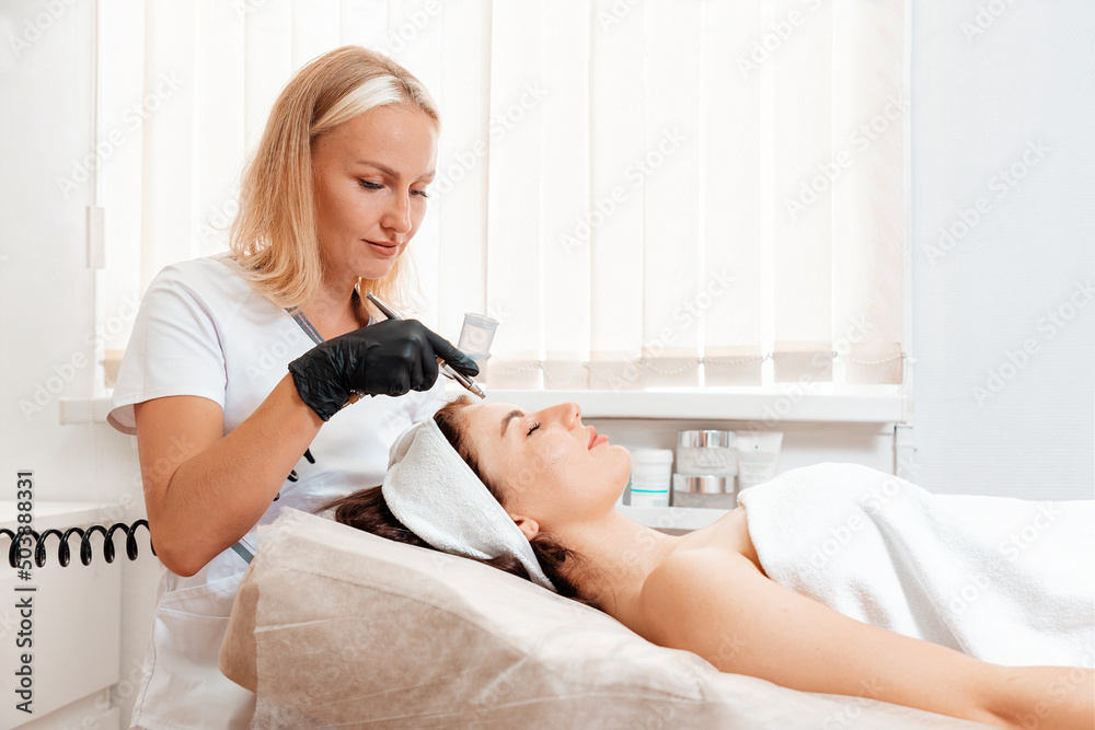 Cosmetologist doing a gas-liquid oxygen water epidermal peeling using hardware apparatus to the client's face. Concept of cosmetology and rejuvenation beauty treatment Cosmetologist doing a gas-liquid oxygen water epidermal peeling using hardware apparatus to the client's face. Concept of cosmetology and rejuvenation beauty treatment