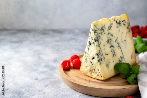 Obraz na płótnie Blue cheese, dor blue or roquefort mold cheese slice on cutting board with basil leaves and rasberries, lifestyle food