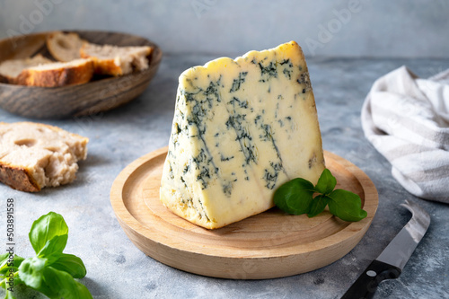 Blue cheese, dor blue or roquefort mold cheese slice on cutting board with basil leaves, lifestyle food.
