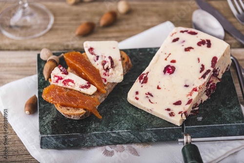 Wensleydale cheese with cranberries, red wine, honey, nuts, raisins on wooden cutting board. Black concrete background. Selective focus.