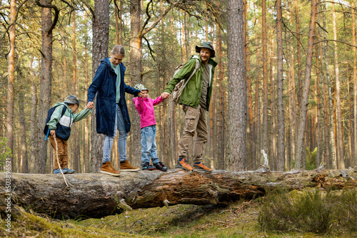 Obraz na płótnie family with children walking on fallen tree in forest