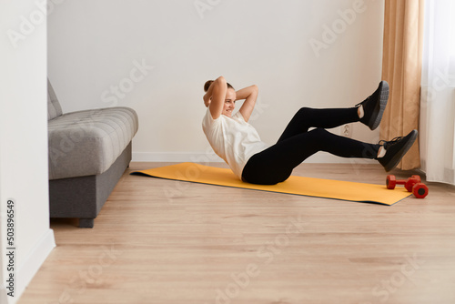 Side view portrait of sporty active woman doing cross training bicycle crunches trains leg muscles and abs, athlete conducts daily training on a mat in the room.
