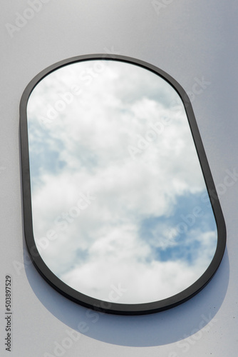 A round or oval mirror with a reflection of the blue sky and white clouds. Close-up. Isolated on a white background