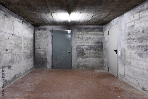 Front view of reinforced concrete wall of a bunker with closed armored door. Scene illuminated by a white neon lamp