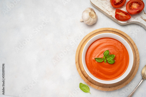 Tomato soup with fresh basil in orange bowl. Bright background. Healthy food concept. Copy space