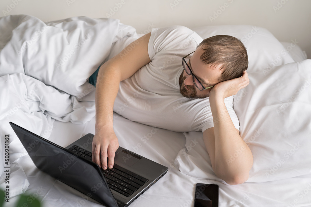 smiling man using Tablet Computer is lying on a bed in the morning. work from home. freelancer. social networks concept. man chatting with friends. smiling man using Tablet Computer is lying on a bed in the morning. work from home. freelancer. social networks concept. man chatting with friends.