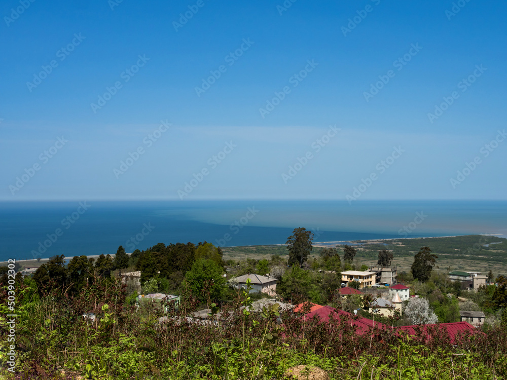 Bird's-eye view of the sea. The place where the muddy river flows into the sea. Confluence of sea and fresh water. Skyline. Blue sky. In the foreground - the roofs of houses (village). Copy space.