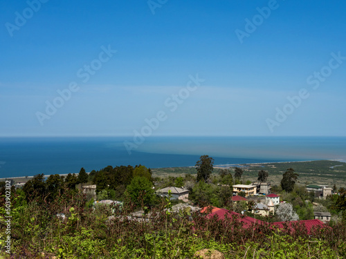 Bird's-eye view of the sea. The place where the muddy river flows into the sea. Confluence of sea and fresh water. Skyline. Blue sky. In the foreground - the roofs of houses (village). Copy space.