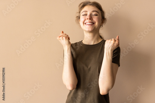 Young woman winning, chanting and rejoicing, shouting supportive and looking hopeful at camera, yearning to win, beige background photo