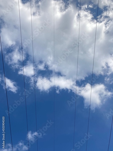 the cables of a power line against the blue sky with white clouds