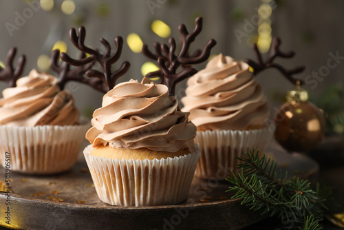 Tasty Christmas cupcakes with chocolate reindeer antlers on wooden tray, closeup