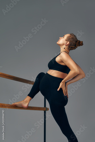 Pregnant woman posing near barre in ballet studio.