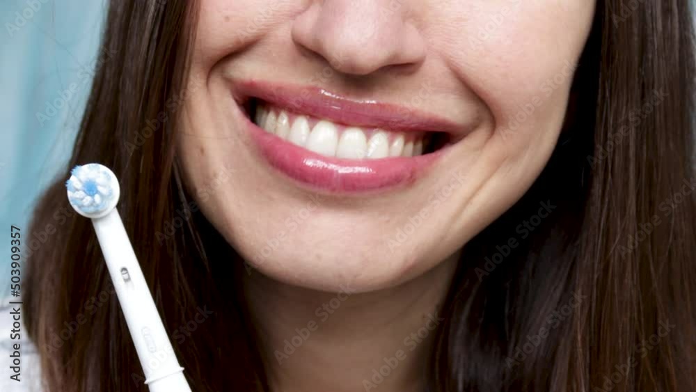 smiling young woman holding electric toothbrush, turning on, rotative