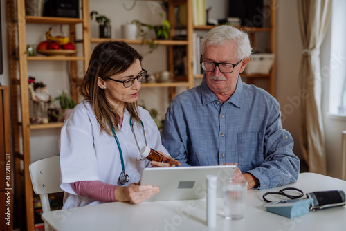 Healthcare worker or caregiver visiting senior man indoors at home, explaining medicine dosage.