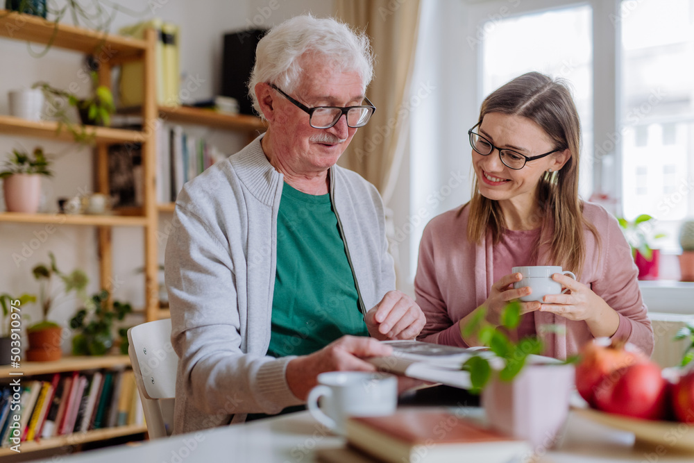 Adult daughter visiting her senior father at home and having coffee together, looking at book. Adult daughter visiting her senior father at home and having coffee together, looking at book.