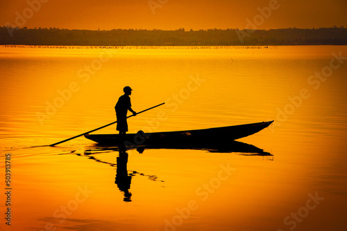 silhouette of one person on a boat on the water with orange sunset backgrownd 