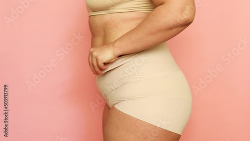 Cropped studio shot of fat overweight woman in special fitness beige shape wear. Fast gain weight with pregnancy. Body health care. Visceral obesity, folds flabs of dehydrated dozed body. Side view