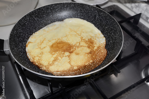 Frying delicious crepe on pan in kitchen, closeup