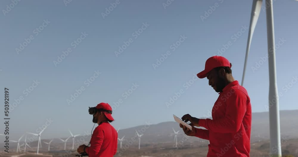 Multiracial engineer men working together on a windmill farm with digital tablet and drone - Renewable energy concept Multiracial engineer men working together on a windmill farm with digital tablet and drone - Renewable energy concept