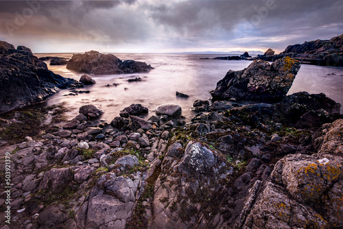Rocky seascape beside Turnberry point lighthouse with cloudy moody sky at coast line