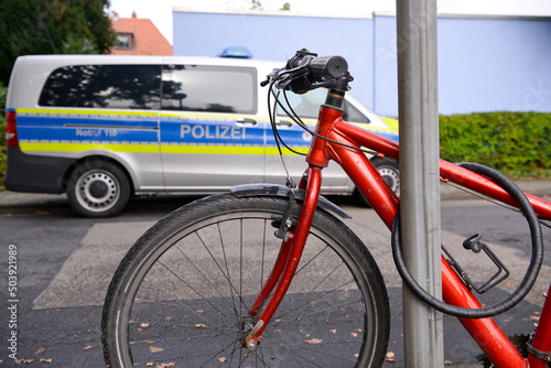 Ein rotes Fahrrad steht angeschlossen an einem Straßenschild, während im Hintergrund ein Polizeiauto parkt. photo