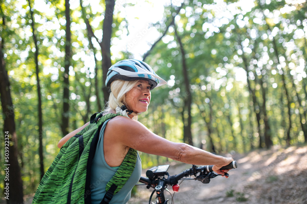Active senior woman biker pushing bike outdoors in forest. Active senior woman biker pushing bike outdoors in forest.