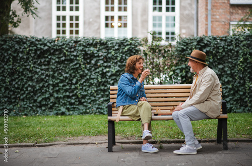 Happy senior couple sitting on bench and playing chess outdoors in park.