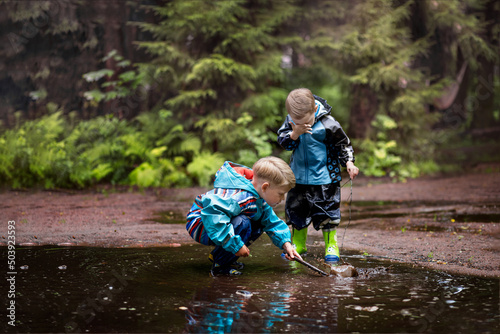 Two little boys are playing in a muddle puddle. There is a reflection in a puddle. Image with selective focus