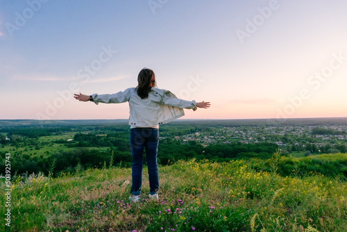 Freedom and rest concept woman spread her hands stands with her back and looks at the view landscape. Relaxation time at the top of the mountain, enjoying the result and achieving success.