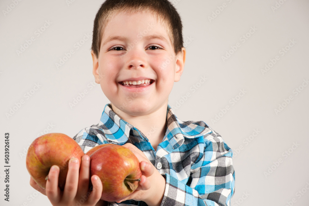 A 4-year-old preschool boy with red apples in his hands is smiling against a white background. A 4-year-old preschool boy with red apples in his hands is smiling against a white background.