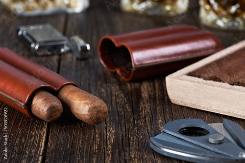 Two Cuban cigars in a leather case with a wooden box on an old brown table top. Glass of whiskey on a blurred background.
