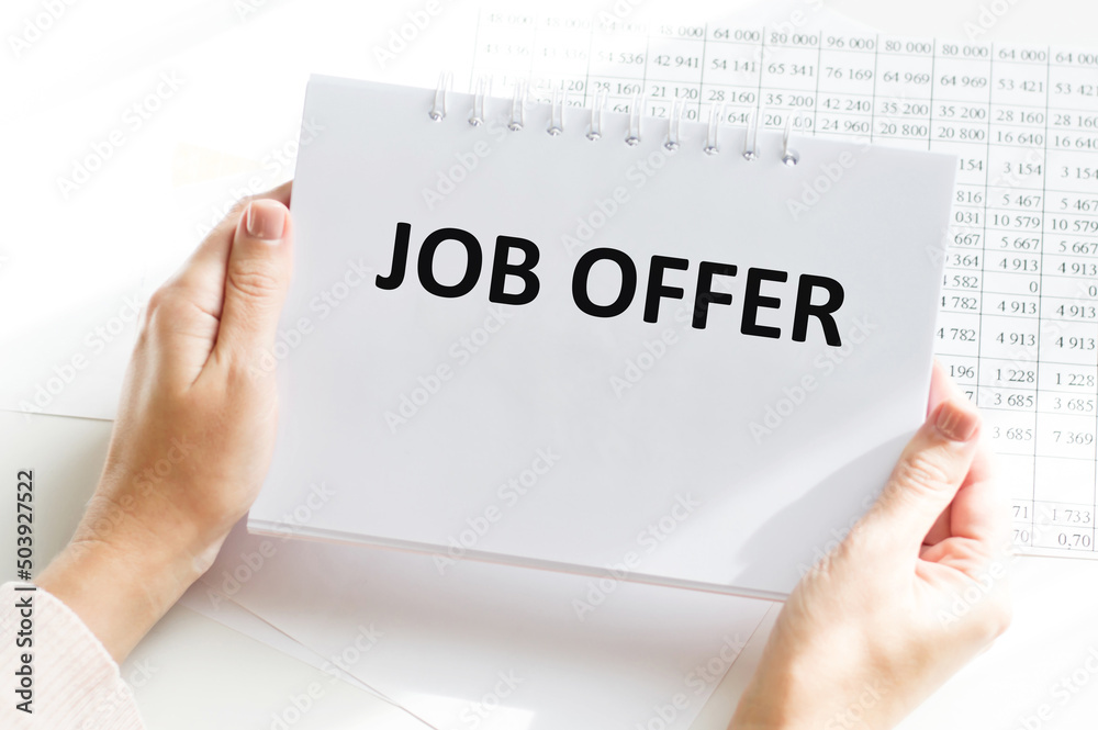 JOB OFFER text on a notebook in the hands of a girl sitting at a table JOB OFFER text on a notebook in the hands of a girl sitting at a table