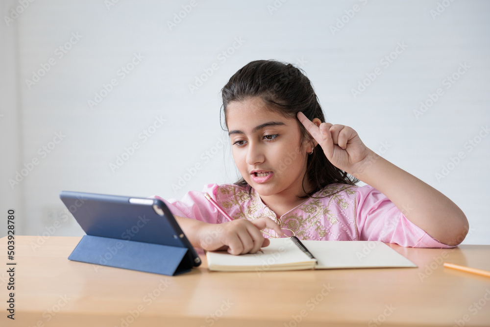 cute Indian girl video call to someone, pointing pose or number one finger sign and looking tablet for online learning class, education concept cute Indian girl video call to someone, pointing pose or number one finger sign and looking tablet for online learning class, education concept