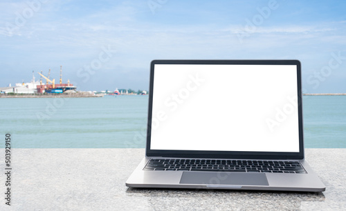 A blank white screen laptop rests on an outdoor marble table. Ideas for business, technology, internet, design, and programmers. Copy space on left. Close-up. Selective focus. Blurred background. © Mdisk
