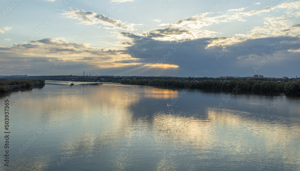 Evening landscape, sunset on the river. Wide river, horizon, clouds are reflected in the water. Sunlight through the clouds.