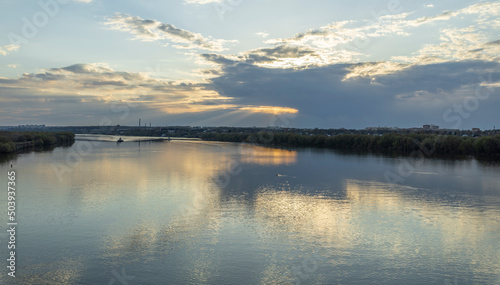 Evening landscape, sunset on the river. Wide river, horizon, clouds are reflected in the water. Sunlight through the clouds.