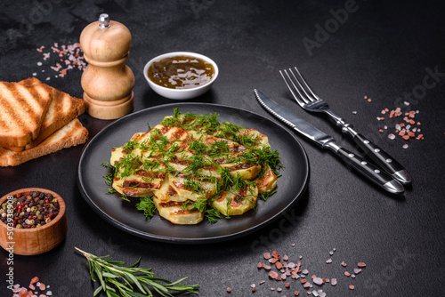 Delicious grilled potato slices with spices and herbs on a black plate