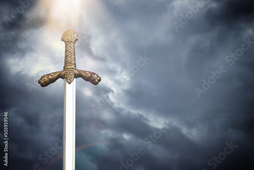 photo of knight sword over stormy skies. Medieval period concept