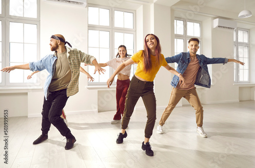 Energetic young people in group in casual wear dance together in studio. Diverse friends or dancer crew perform train for contest or competition. Hobby and entertainment concept.