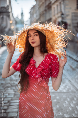 Cute girl with straw hat and red dress walk on old city street