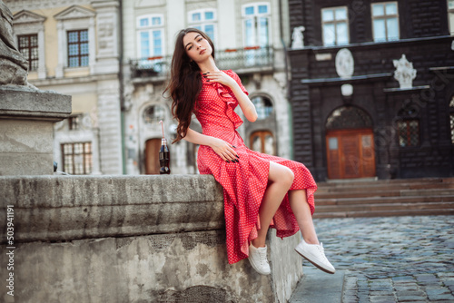 Attractive girl in red polka-dot dress with soda on old city background
