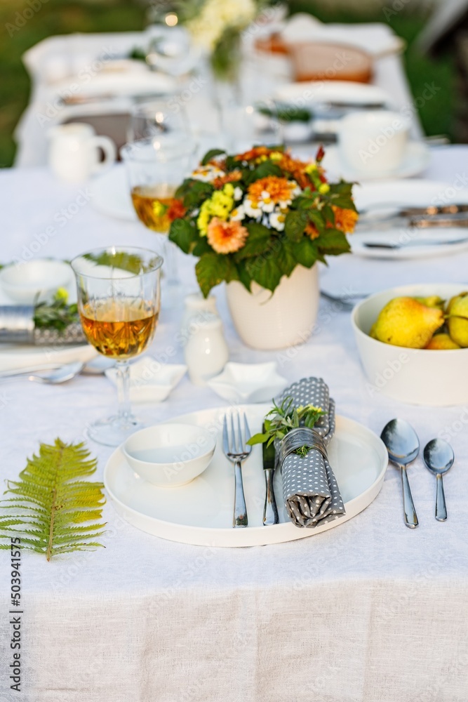Elegant table setting with white dishes on a white linen tablecloth. Fruits, drinks in crystal glasses. Summer holiday table set up. Outdoor eating on a table in the garden. Vertical shot Elegant table setting with white dishes on a white linen tablecloth. Fruits, drinks in crystal glasses. Summer holiday table set up. Outdoor eating on a table in the garden. Vertical shot
