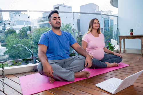 couple of man and pregnant woman sitting meditating in online yoga class.