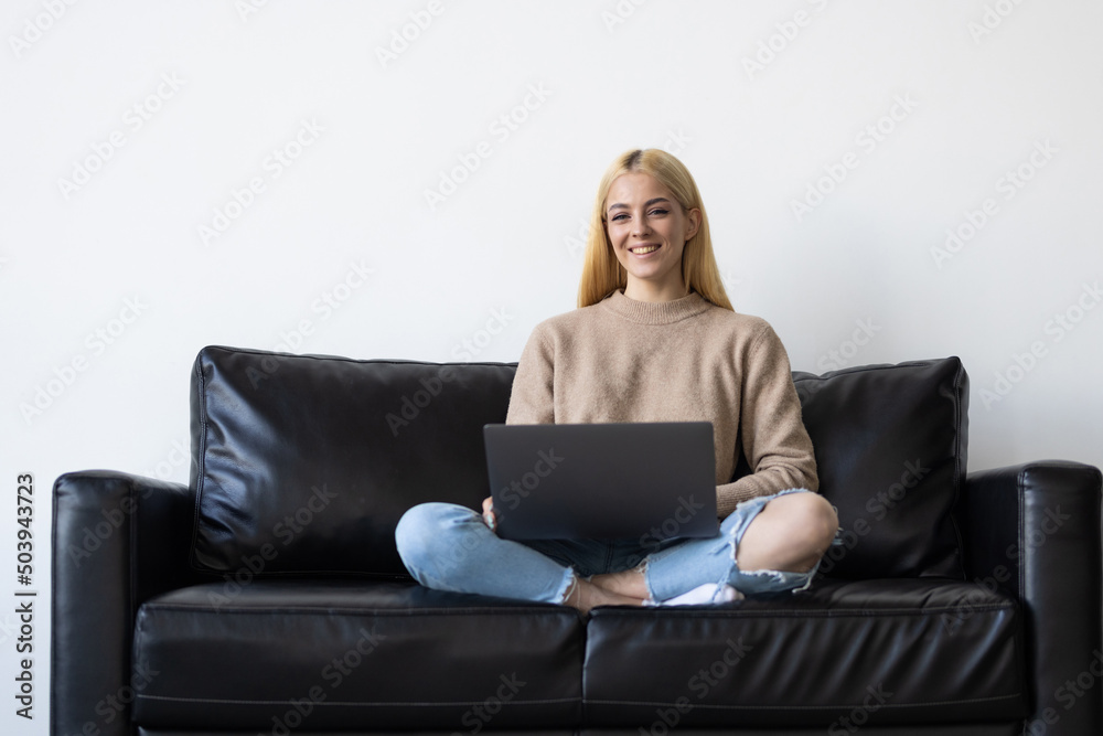 Young woman happy positive smile sit couch look browse laptop indoors Young woman happy positive smile sit couch look browse laptop indoors