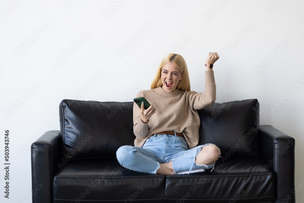 Excited woman checking phone online content celebrating good news sitting on a couch in the living room at home