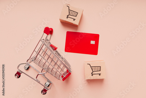 Credit card with shopping cart and delivery boxes on pink background. Shopping by cart